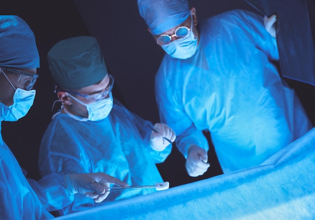 Group of surgeons at work in operating theater toned in blue Medical team performing operation