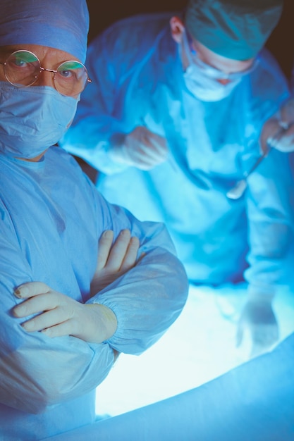 Group of surgeons at work in operating theater toned in blue Medical team performing operation