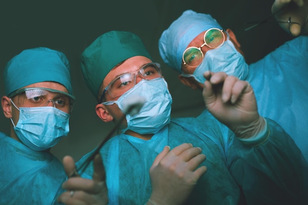 Group of surgeons at work in operating theater toned in blue Medical team performing operation