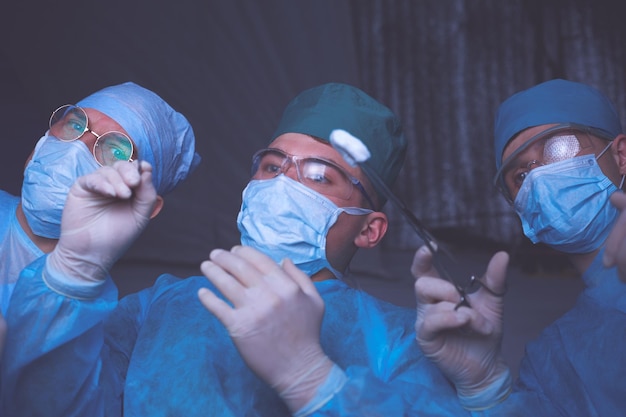 Group of surgeons at work in operating theater toned in blue Medical team performing operation