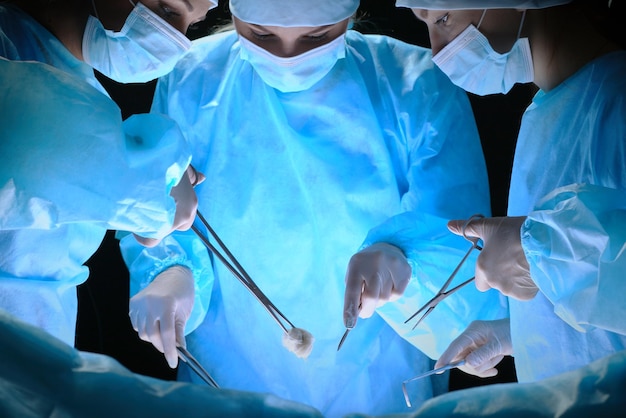 Group of surgeons at work in operating theater toned in blue. Medical team performing operation