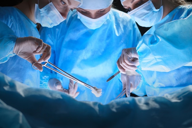 파란색으로 톤된 수술실에서 일하는 외과의사 그룹
