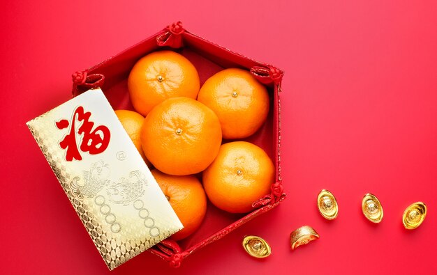 Photo group of tangerine in tray and envelope packet ang pow with gold ingots on red table top