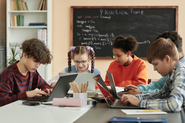 Group of teen children using laptops in school classroom studying