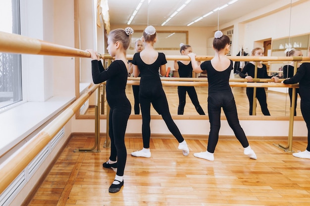 Foto un gruppo di ragazze adolescenti in abiti sportivi che fanno allungamenti delle gambe vicino alla sbarra. ginnastica ritmica.