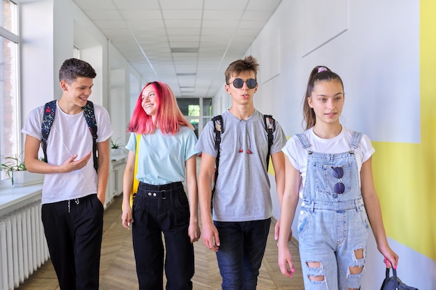 Group of teenage students walking together along school\
corridor, schoolchildren smiling and talking. education, high\
school, adolescence concept