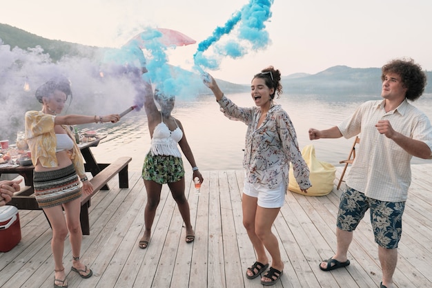 Group of teenagers dancing on a pier outdoors among colored smoke