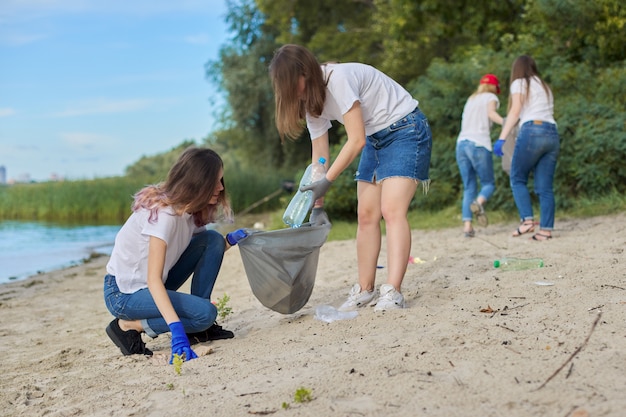 Group of teenagers on riverbank picking up plastic trash in bags