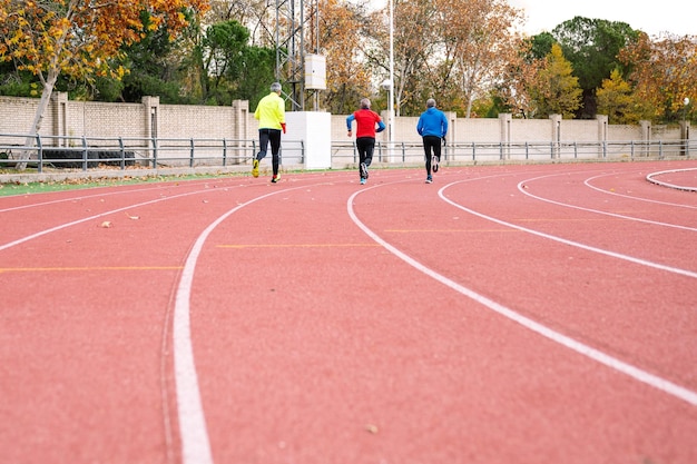 Photo group of three active senior athletes jogging on a red track