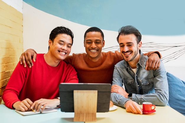 Group of three male friends sitting at table in a cafe looking at something on tablet device