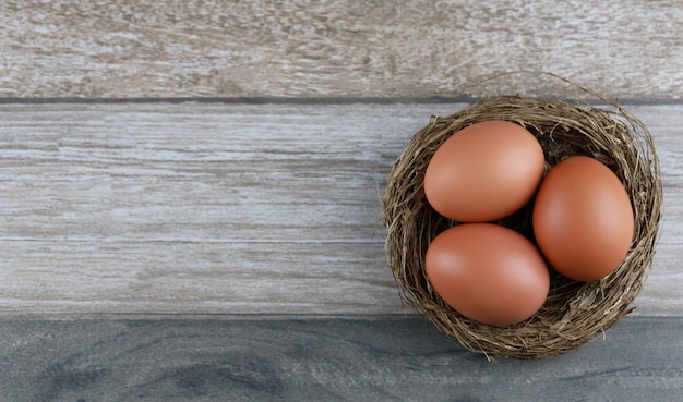 Raggruppi tre uova di gallina naturali dai prodotti di fattoria nel nido dell'uccello sulla tavola di legno d'annata. immagine pubblicitaria concetto di pasqua o cibo con spazio libero.