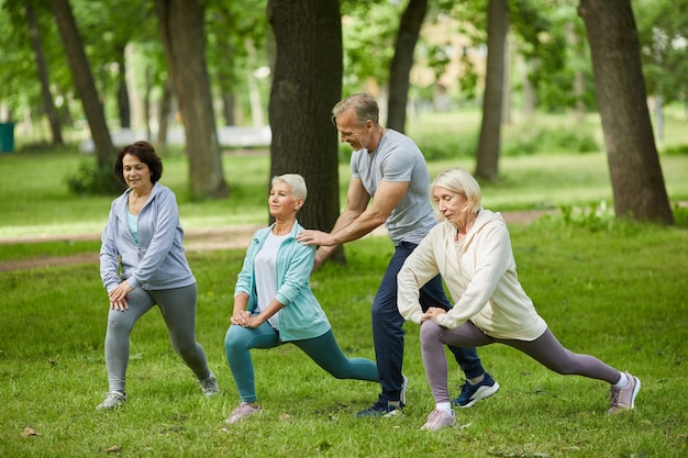 Group of three senior women spending morning together in park doing exercises with their trainer helping them