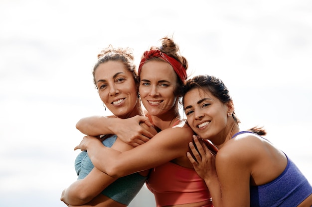 Photo group of three woman warms up in park before jogging healthy lifestyle concept sporty females friends having fun and doing different stretching exercises in summer park