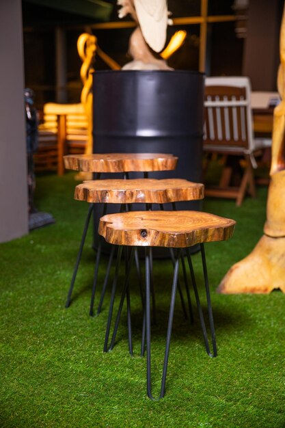 A group of three wooden stools sit on a green grass covered area with a black barrel in the background