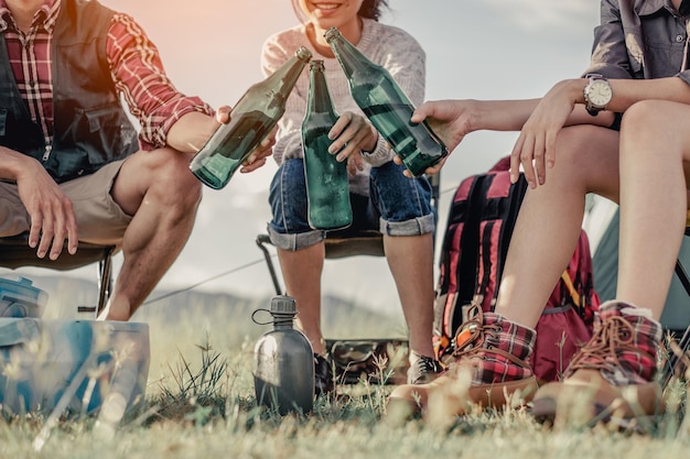 Gruppo di turisti che tintinnano bottiglie di birra in campeggio.avventura, viaggi, turismo, amicizia e concetto di persone.