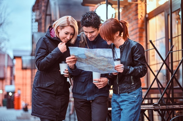 Foto gruppo di turisti che cercano un posto sulla mappa vicino a un caffè all'esterno.