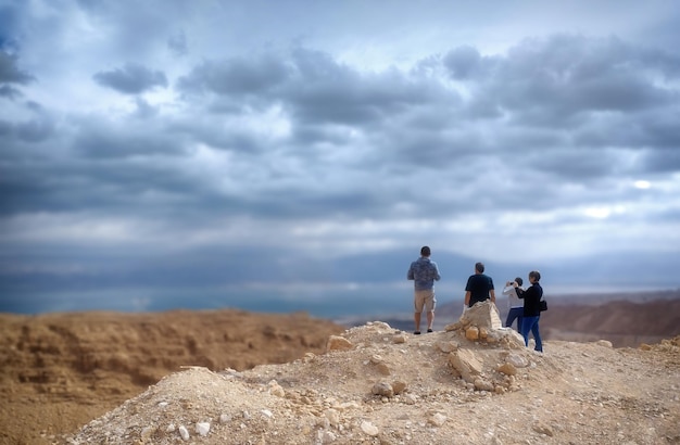 A group of tourists stand on a hill and look into the distance taking pictures on their phones