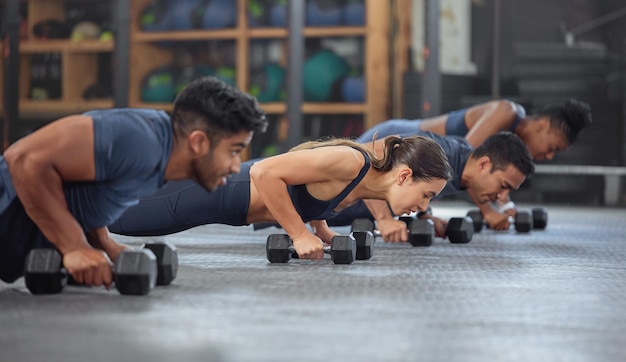 Group training dumbbell pushup and row exercise workout and fitness in a gym class Sporty strong and active people with endurance energy and wellness completing a sports challenge