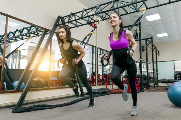 Group training with loops in gym, two fitness women doing cross fit