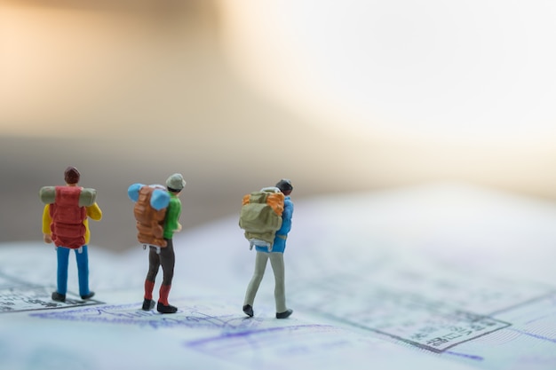 Photo group of traveler miniature figures with backpack walking on passport with immigration stamps.