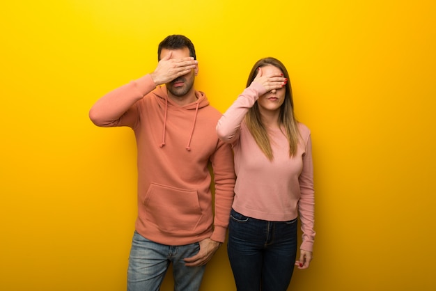 Group of two people on yellow background covering eyes by hands