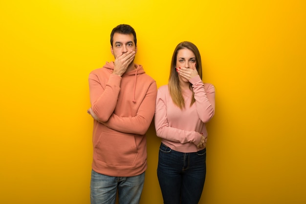 Group of two people on yellow background covering mouth with hands