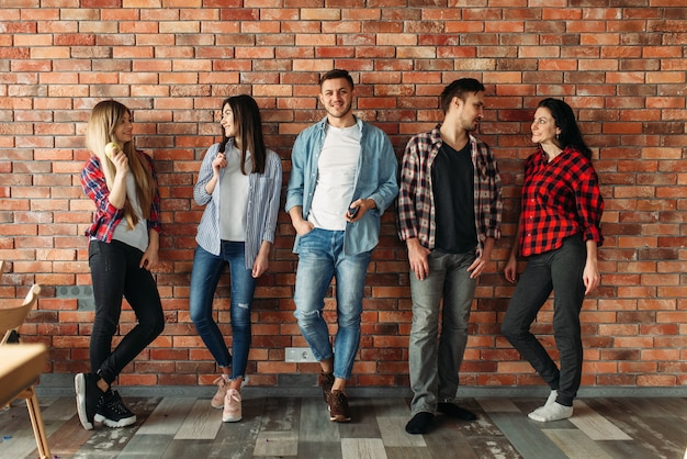 Gruppo di studenti universitari in piedi presso il muro di mattoni. pose giovanili delle scuole superiori