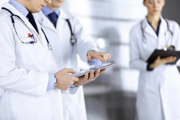 Group of unknown doctors use a computer tablet to check up some
medical names records, while standing in a hospital office.
physicians ready to examine and help patients. medical help,
insurance in he