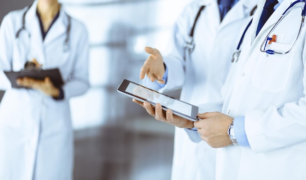 Group of unknown doctors use a computer tablet to check up some medical names records while standing in a hospital office Physicians ready to examine and help patients