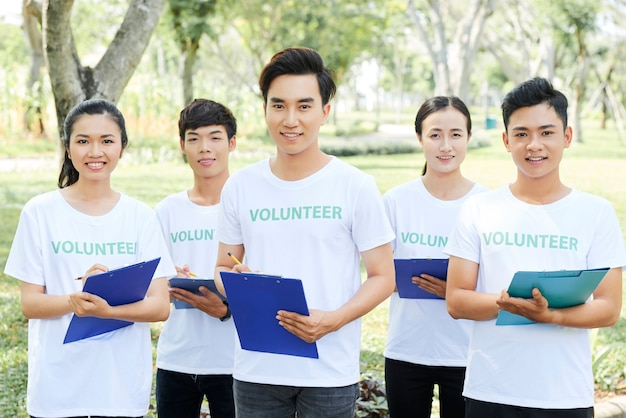 Group of volunteers with their leader standing in park with clipboard in hands and looking at camera