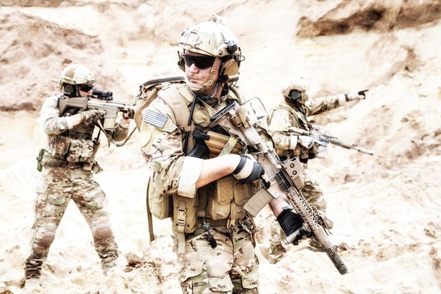 Group of well equipped US army commandos armed with assault rifles, moving through sandy terrain or desert. Military reconnaissance team secret operation, special forces mission on enemy territory