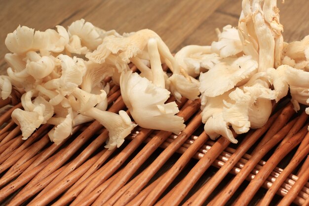 Photo a group of white oyster mushroom on wicker basket on brown wooden table ready to cook in the kitchen