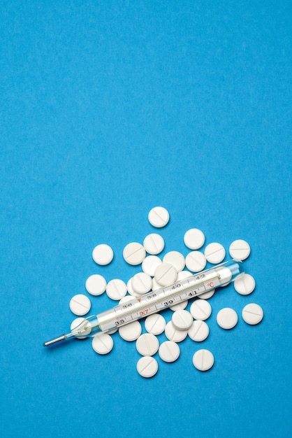 group of white pills or tablets and mercury thermometer on blue background