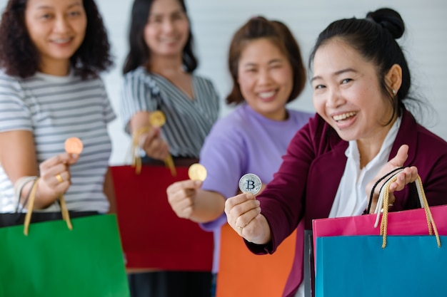 Group of woman holding crypto money coins and a variety of colors of shopping bags on hand. Concept of cryptocurrency payment and digital money using in real life of modern people.