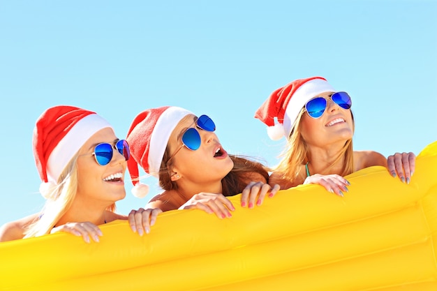 group of women in bikini and Santa's hats holding mattress on the beach