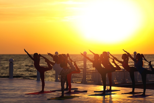 The group of women doing yoga at sunrise near the sea