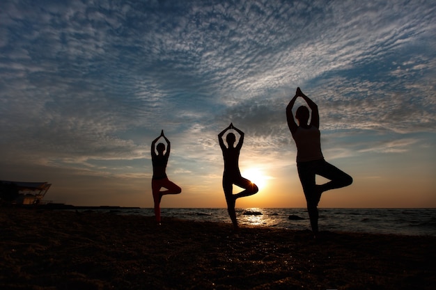 The group of women doing yoga at sunrise near the sea