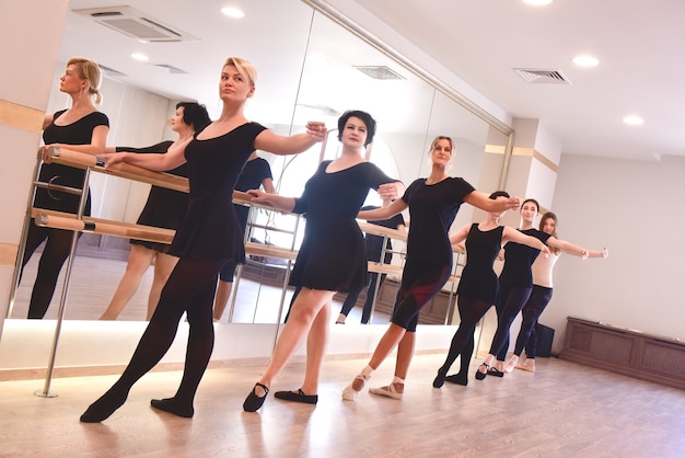 Un gruppo di donne esegue esercizi di balletto alzando le braccia usando la barra in palestra