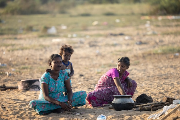 A group of women sit on the ground in front of a dirty trash can.