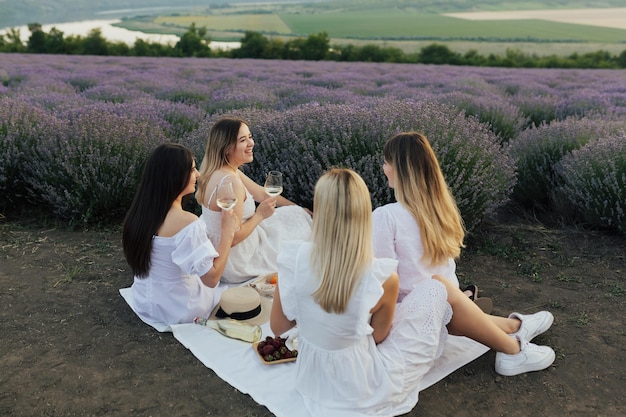 A group of women in white dresses are sitting on a blanket in a field of lavender.