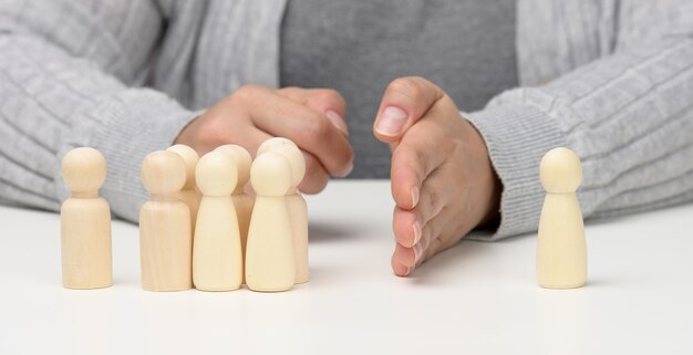 A group of wooden figures stands opposite one figure, with a hand between them. The concept of reconciliation of opponents, the end of bullying, the search for a compromise