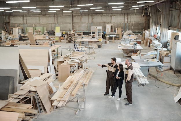 Группа рабочих современной фабрики обсуждает материалы для производства мебели, в то время как менеджер по продажам указывает на них на встрече