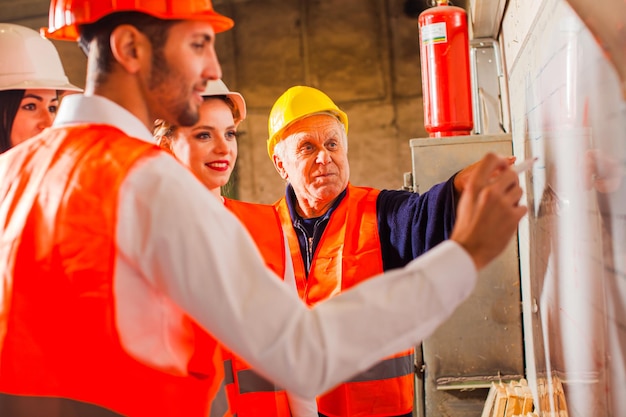 The group of workers in overalls are standing next by the flip chat four engineers make up the work schedule