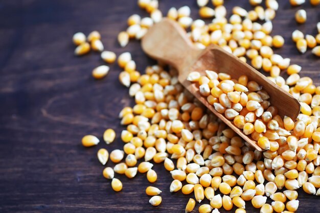 Группа желтых сырых зерен сладкой кукурузы. Ингредиент семян зерновых культур золотое зерно кукурузы. Деревянный стол спелый фон попкорн.
