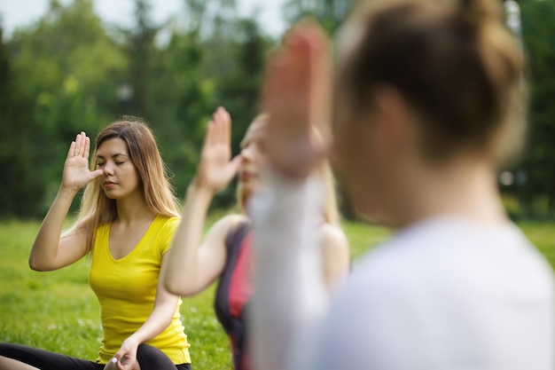 A group of yoga sportsmen performs breathing exercises in park, summer