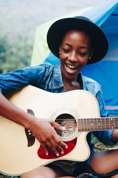 Group of young adult friends in camp site playing guitar and singing together outdoors recreational 