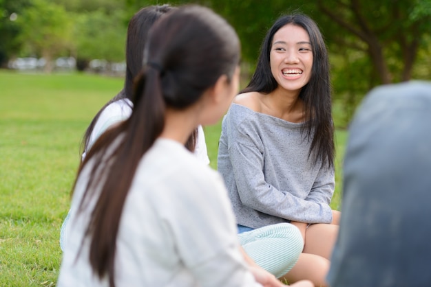 屋外の公園で一緒にぶらぶらしてリラックスしている若いアジアの友人のグループ