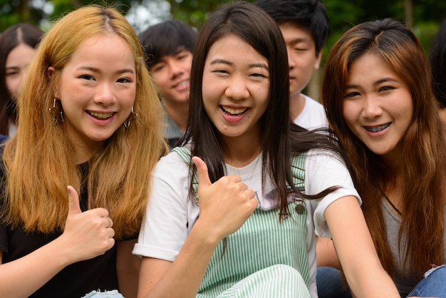 屋外の公園で一緒にぶらぶらしてリラックスしている若いアジアの友人のグループ