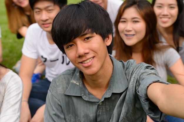 Photo group of young asian friends hanging out and relaxing together at the park outdoors