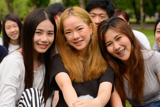 Group of young Asian friends hanging out and relaxing together at the park outdoors